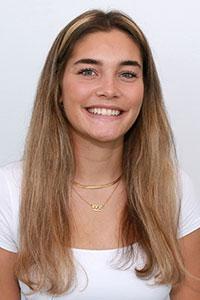 woman with dark blonde hair wearing a white shirt and gold necklaces