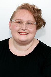 person with short strawberry blonde curly hair wearing glasses and a black shirt